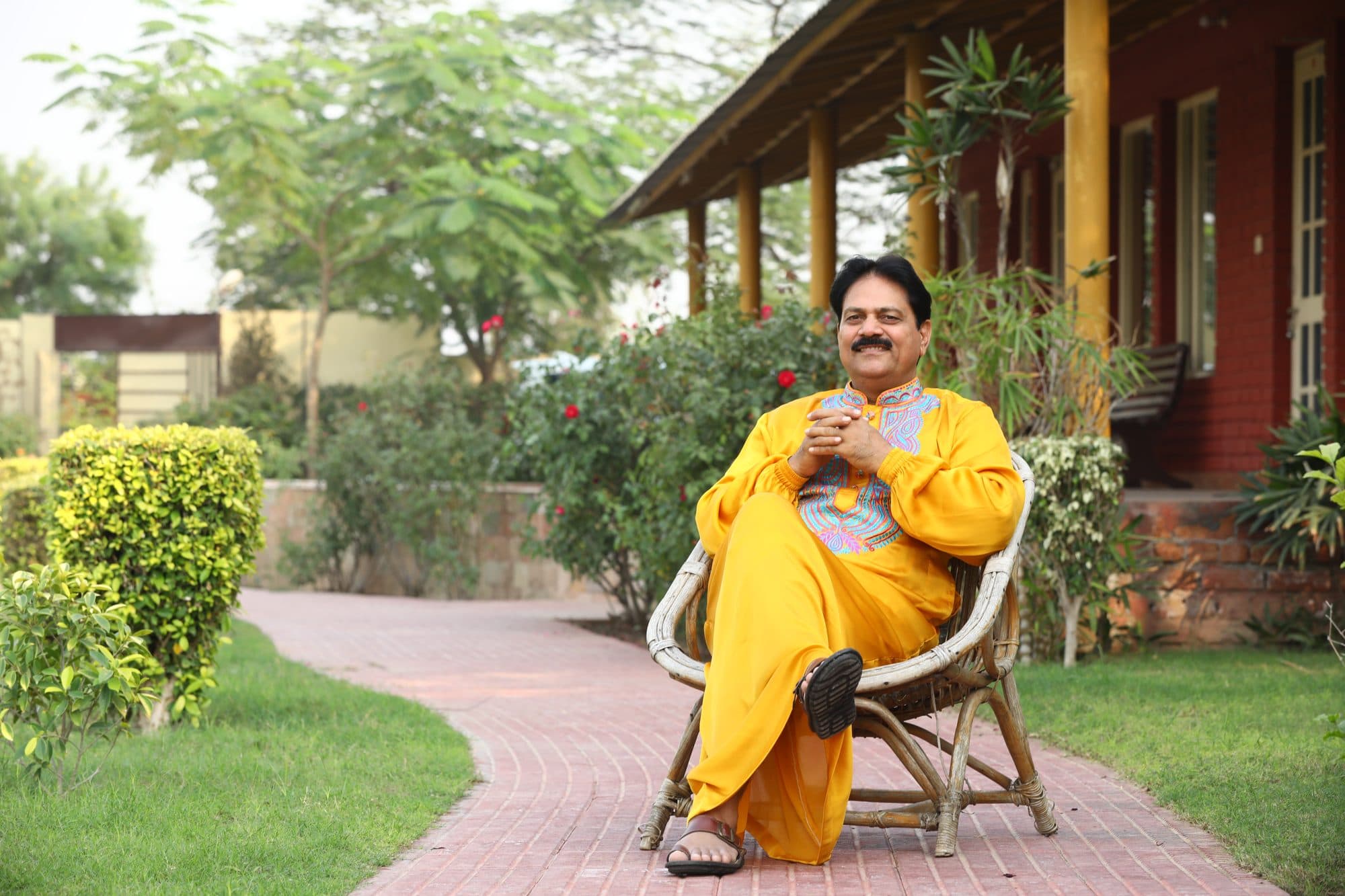 Anando in a gold kurta, seated in a garden and smiling